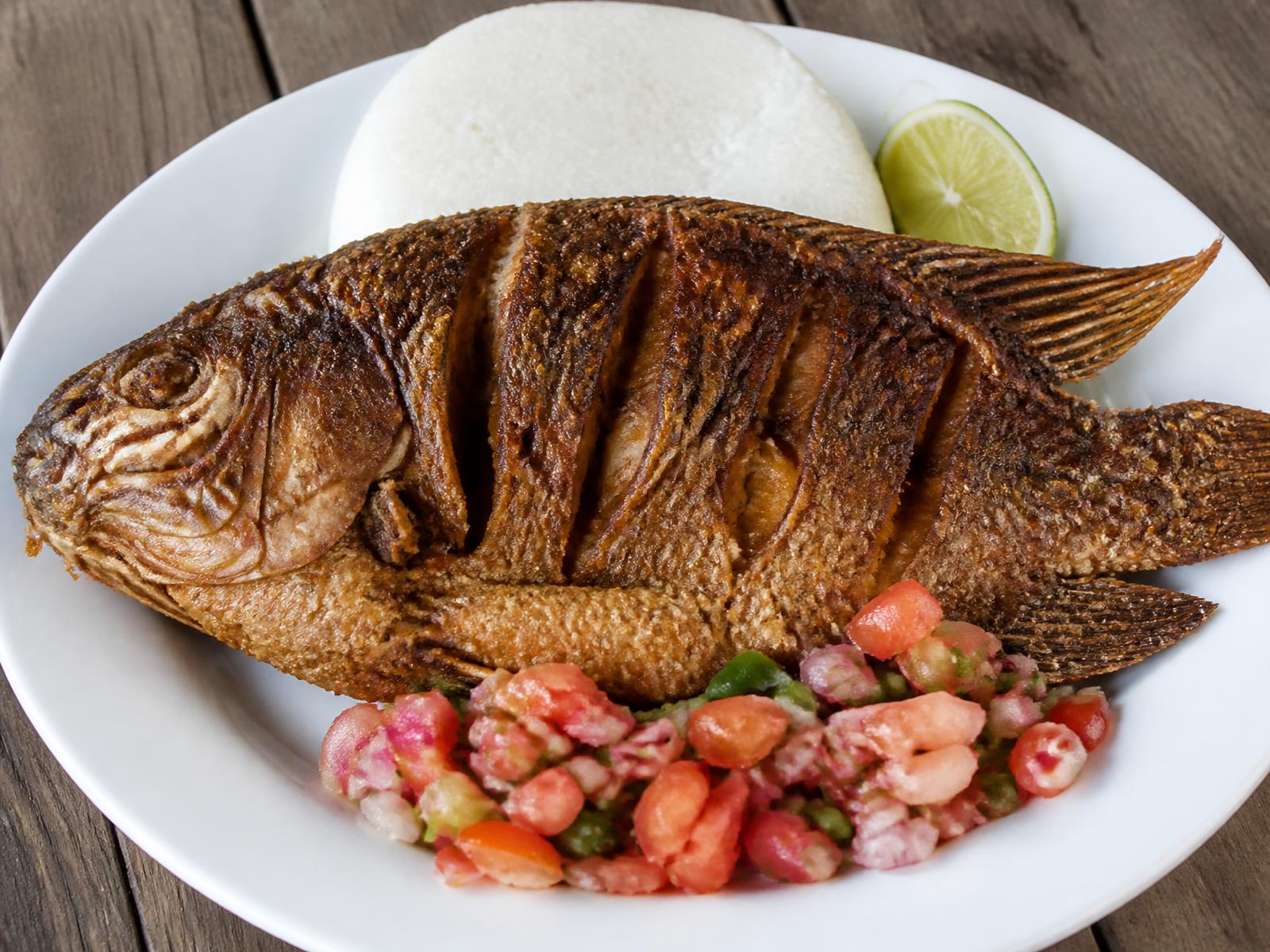 Golden crispy fried tilapia served with ugali, kachumbari and lime